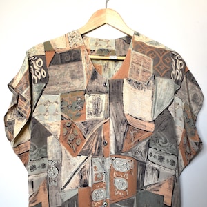 Puede incluir: Una camisa de manga corta con botones y un patrón geométrico en tonos marrones, beige y grises. La camisa tiene cuello en V y cierre de botones en la parte delantera.