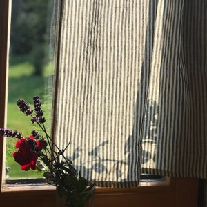 black stripe lightweight linen curtain panel allows light to pass through while giving privacy. Bottom half of window is covered with simple cafe style curtain. a red rose in vase enhances the colours of the curtain