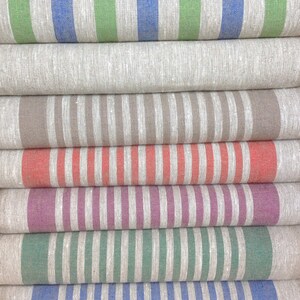 May include: A stack of folded linen fabric rolls with vertical stripes in various colors. The colors include blue, green, gray, brown, coral, purple, and white. The fabric appears to be a natural fiber, possibly linen or cotton.