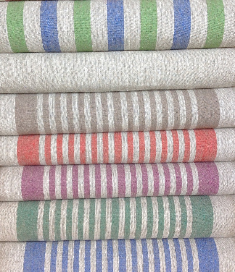 May include: A stack of folded linen fabric rolls with vertical stripes in various colors. The colors include blue, green, gray, brown, coral, purple, and white. The fabric appears to be a natural fiber, possibly linen or cotton.