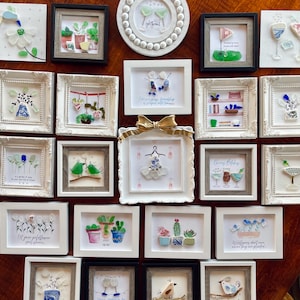 May include: A collection of framed art pieces, each featuring unique designs. The artwork includes images of plants, birds, and cocktail glasses, crafted with various materials. Some frames have text, such as "Cheers Bitches" and "Pot Head."