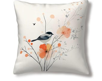 May include: A white throw pillow with a watercolor design of a bird perched on a branch with orange flowers. The background is a light cream color.