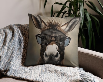 May include: A brown and white donkey wearing blue-tinted glasses on a throw pillow. The pillow has a light brown background.