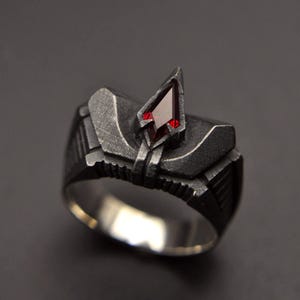 May include: A silver ring with a geometric design and a red gemstone in the center.