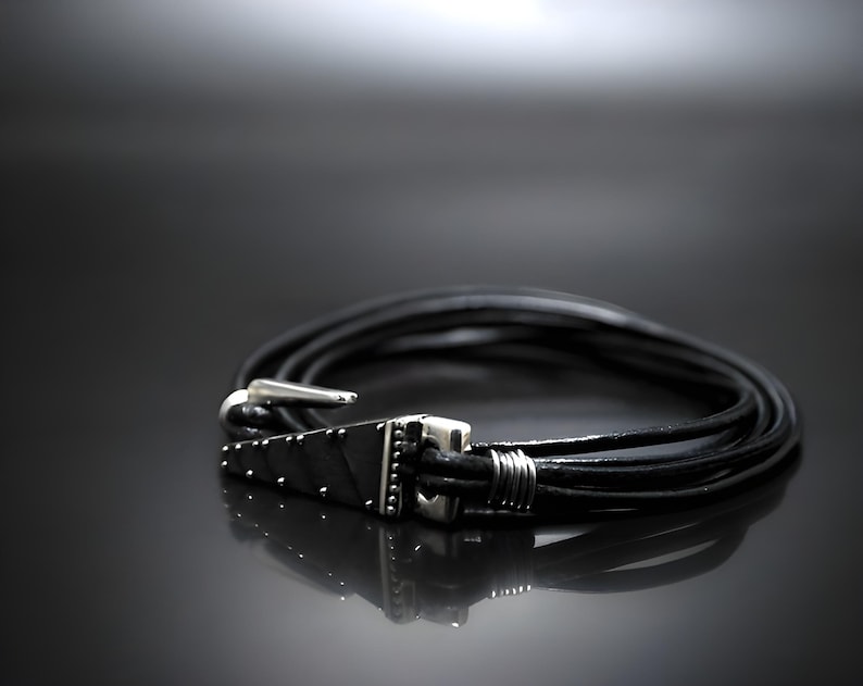 Pu&ograve; includere: Un braccialetto in pelle nera con una chiusura argentata e un design geometrico. Il braccialetto &egrave; a strati e ha una chiusura a gancio.