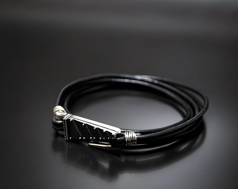 Pu&ograve; includere: Un braccialetto in pelle nera con una chiusura argentata. La chiusura ha un design testurizzato.