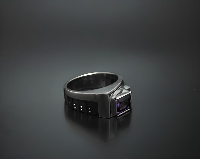 K&ouml;nnte beinhalten: Ein silberner Ring mit einem schwarzen Band und einem violetten Edelstein. Das Band hat ein strukturiertes Design.