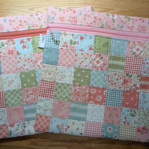 Pode incluir: Duas bolsas com zíper de patchwork com um padrão floral e geométrico em tons de rosa, azul e verde. As bolsas têm um zíper rosa e uma parte superior com estampa floral. Uma bolsa tem um pingente preso ao zíper.