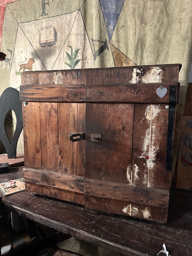 May include: A wooden cabinet with two doors, painted brown. The cabinet has a heart-shaped metal tag on the right door. The cabinet is sitting on a wooden table.