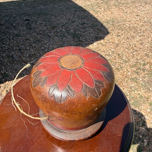 May include: A round, brown decorative object with a red floral design on top. The object sits on a dark brown, round table. A natural fiber cord is attached to the object. The object has a decorative base.