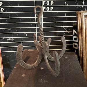 May include: A rustic metal coat rack made from four horseshoes and a twisted metal hook. The rack is mounted on a dark brown surface.