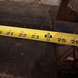May include: A yellow measuring tape with black markings reads 21 to 26 inches. The tape is placed on a dark brown wooden surface.