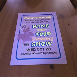 May include: A purple flyer on a wooden table promotes a "Wine and Food Sampling Show" on Wednesday, October 28th. The flyer includes the text "Coming to the O'Club" and "Discover new products and Trends at our..."