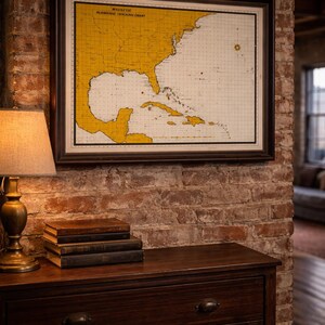 May include: A framed vintage map of the southeastern United States and the Caribbean, labeled "Magnetic Hurricane Tracking Chart." The map is yellow and white, set in a dark brown frame, and hangs on a brick wall above a wooden dresser.