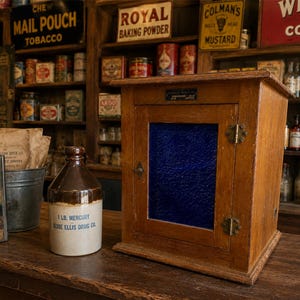 May include: A wooden cabinet with a single door featuring a textured cobalt blue glass panel, brass hinges, and a small metal latch. Beside it sits a cylindrical ceramic jug labeled 1 LB. MERCURY JESSE ELLIS DRUG CO. in blue text.