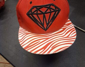 Gorra snapback Diamond Supply Co. con estampado de cebra rojo, visera y logo negro, estilo streetwear.