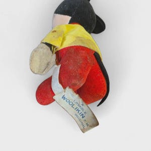 K&ouml;nnte beinhalten: Vintage Mickey Mouse Pl&uuml;schtier. Das Spielzeug hat einen schwarzen Kopf und Ohren, ein gelbes Hemd, rote Shorts und beige Handschuhe. Ein Etikett lautet "Woolikin Original". Das Pl&uuml;schtier ist in einem gut erhaltenen Zustand.