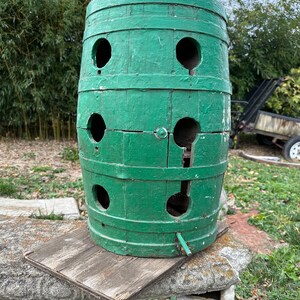 May include: A green wooden barrel with multiple circular holes cut into it. The barrel is sitting on a wooden platform.