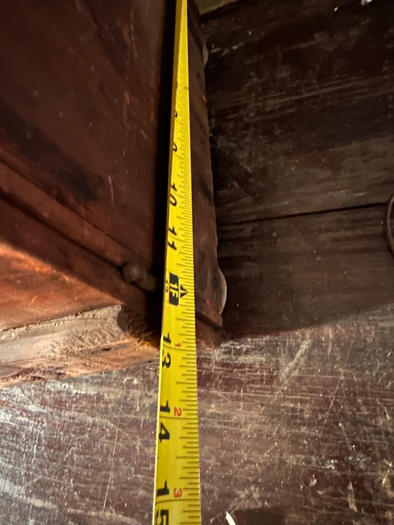 May include: Close-up of a yellow measuring tape with black markings, showing measurements from 10 to 15 inches. The tape is positioned against a dark brown wooden surface.