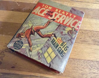 May include: A vintage book titled "Ace of Service and the Big Brain Gang" by Tom Beatty. The cover features a dynamic illustration of a man in a brown suit falling from a building. The book is a "Better Little Book" edition.