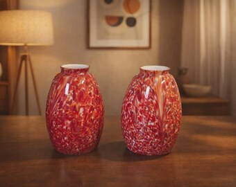 May include: Two decorative vases with a speckled red and white pattern. The vases have a rounded shape with a wide base and a narrow opening. The interior of the vases is white. These vases would be a great addition to any home decor.