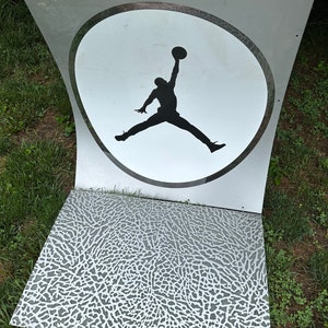 May include: A white and black silhouette of a basketball player jumping in a circle on a clear acrylic sign. The sign is on a gray and white textured surface.