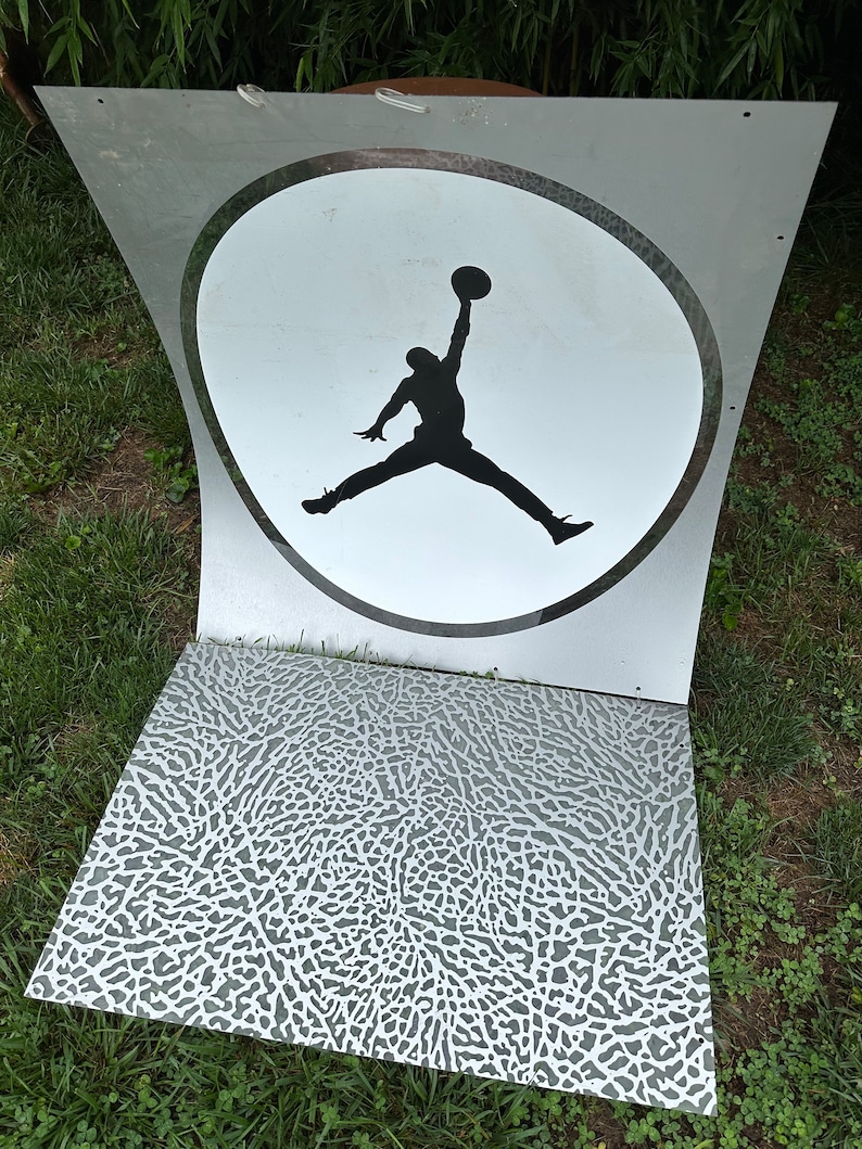 May include: A white and black silhouette of a basketball player jumping in a circle on a clear acrylic sign. The sign is on a gray and white textured surface.