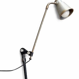 May include: A vintage-style industrial desk lamp featuring a black circular base and vertical support, a long thin brass-toned arm, and a flexible neck connected to a weathered silver-toned conical shade containing a single white light bulb.