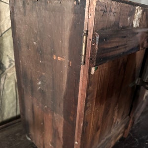 May include: A dark brown wooden cabinet with a single door and a brass hinge. The cabinet has a handwritten inscription on the side that reads "A.F."