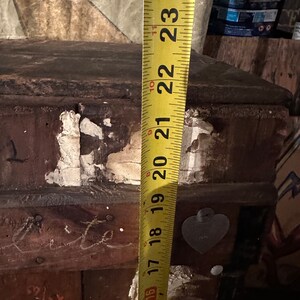May include: A yellow measuring tape with black markings is extended to 23 inches. The tape is attached to a wooden surface with a heart-shaped sticker.