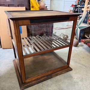 May include: A rectangular wooden display case with a glass front and top. The front glass features the white script text "Schultze" and a dark metal plaque at the top reads "Butter-Krust Bread". The interior includes a slatted wooden shelf.
