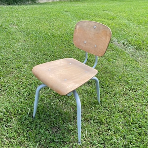 May include: A light gray metal chair with a wooden seat and back. The chair is sitting on a grassy lawn.