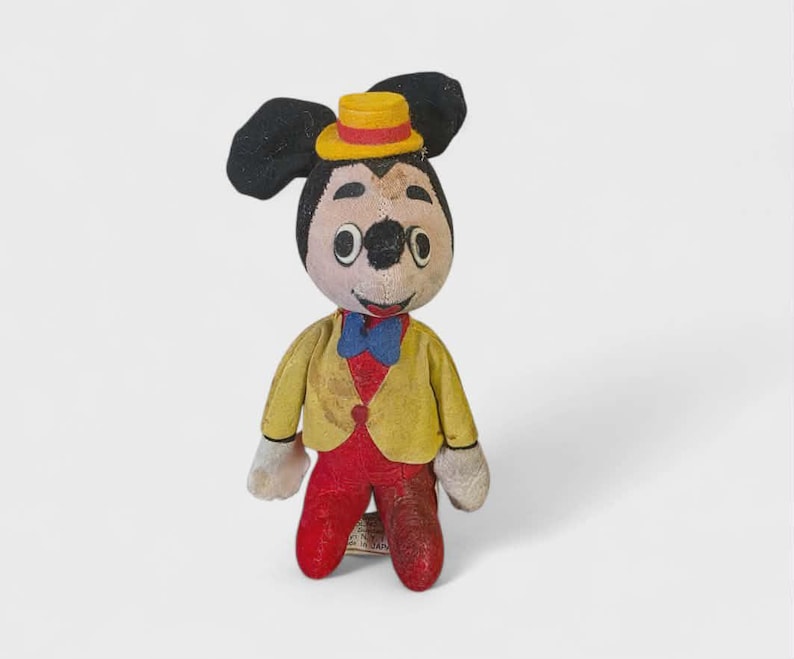 K&ouml;nnte beinhalten: Vintage Mickey Mouse Pl&uuml;schtier. Die Figur hat schwarze Ohren, einen gelben Hut mit rotem Band und eine gelbe Jacke &uuml;ber einer roten Weste. Sie hat rote Hosen, wei&szlig;e Handschuhe und eine blaue Fliege.
