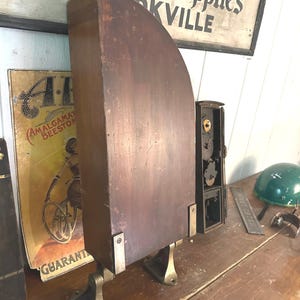 May include: A vintage wooden wall-mounted display stand with brass feet and metal accents. The stand has a curved top and is designed to hold items like small tools or other collectibles.