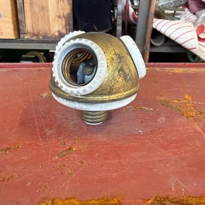 May include: A vintage brass-toned metal light bulb socket adapter featuring three individual bulb sockets arranged around a central dome. The unit includes white plastic threaded rings and a standard screw-in base for electrical installation.