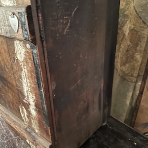 May include: A vintage wooden cabinet with a dark brown finish and a metal heart-shaped tag on the front. The cabinet has a distressed look with visible wear and tear.