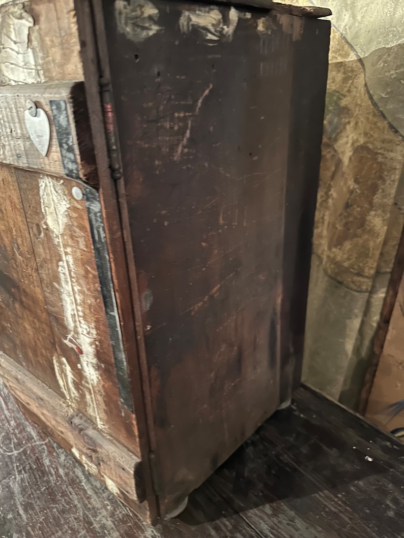 May include: A vintage wooden cabinet with a dark brown finish and a metal heart-shaped tag on the front. The cabinet has a distressed look with visible wear and tear.