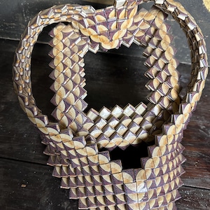 May include: A decorative object made of small, square tiles with a geometric pattern. The tiles are arranged in a circular shape, creating a three-dimensional effect. The tiles are a combination of cream, brown, and purple.