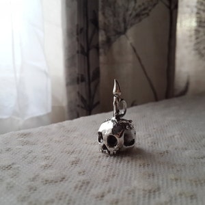 May include: A silver skull charm with a candle on top. The charm is detailed and has a realistic look.