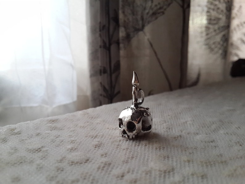 May include: A silver skull charm with a candle on top. The charm is detailed and has a realistic look.