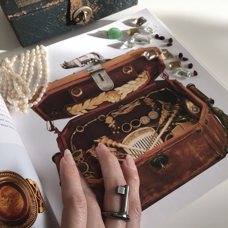 May include: A vintage wooden box with a brass latch, filled with various trinkets and tools. The box is open and a hand is wearing a silver ring with a geometric design.