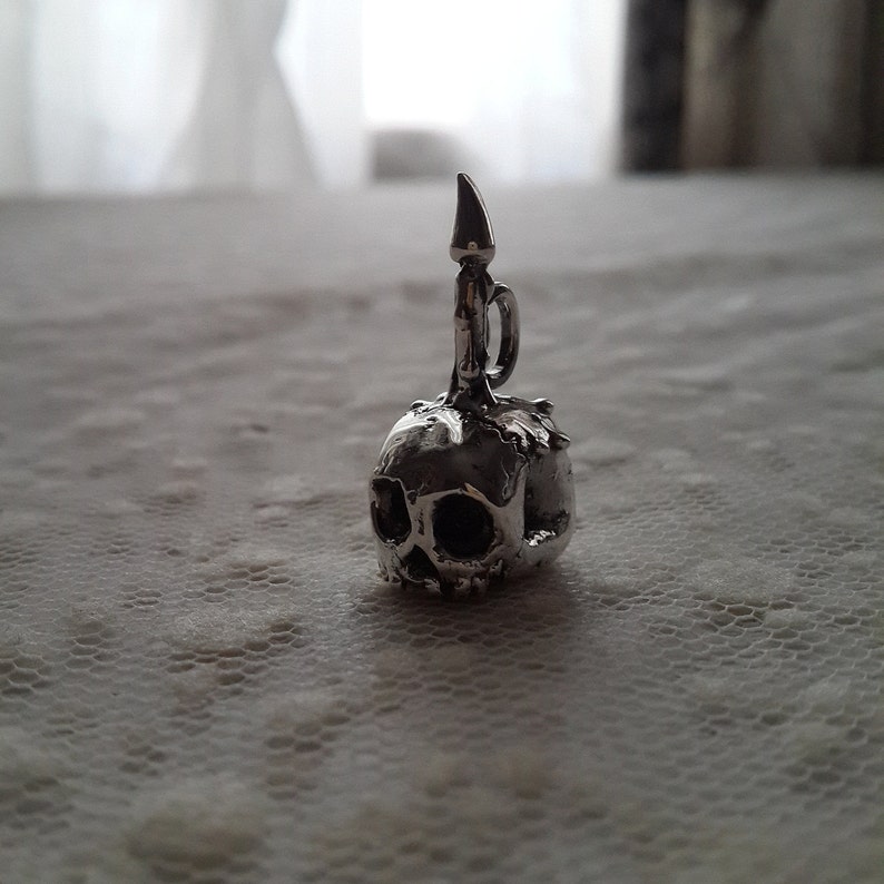 May include: A silver skull charm with a candle on top. The skull has detailed features and a textured surface.