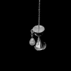 May include: A silver pendant necklace with a pear-shaped pearl charm. The pendant is shaped like a goblet with a wide, round top and a narrow, pointed base.