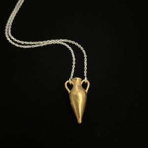 May include: A gold-colored necklace with a pendant shaped like a small, detailed amphora or ancient Greek vase.