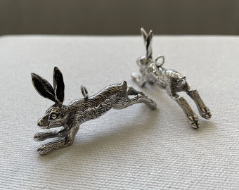 May include: Two silver hare charms, each depicting a hare in a leaping pose. The charms are detailed with textured fur and have a loop for attaching to a necklace or bracelet.