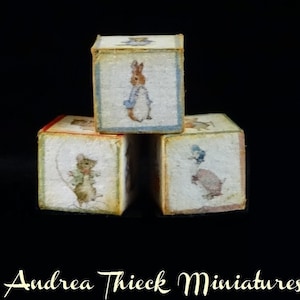 May include: Three wooden blocks stacked on top of each other. Each block features a different illustration from the Peter Rabbit series. The top block features Peter Rabbit, the middle block features a mouse, and the bottom block features a duck.