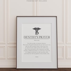 May include: A framed print with the text "DENTIST'S PRAYER" and a caduceus symbol. The prayer is printed in black on a white background, within a black frame. The words "FRAMING NOT INCLUDED" are at the top of the print.