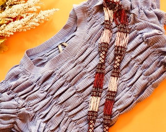 May include: A light blue, textured,  ruched top with a long, beaded necklace in shades of brown, white, and pink.