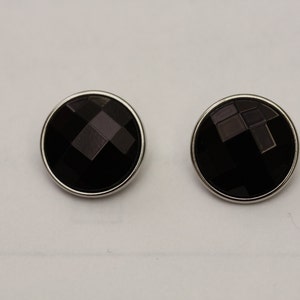 May include: Two round, black faceted buttons with a silver-colored metal rim. The buttons have a geometric design and are set against a white background. These buttons are suitable for various sewing and craft projects.