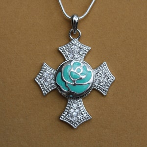 May include: Silver-toned cross pendant necklace with a turquoise rose design at the center. The cross features sparkling clear crystals and is suspended from a delicate silver chain. A stylish piece of jewelry.